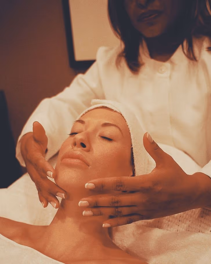 A practitioner's hands gently cradling a client's face during a facial treatment at the studio